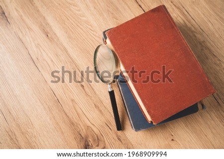Top view magnifying glass on a stack of books on wooden table,The concept of study research searching and reading.