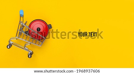 Miniature shopping trolley with pan on yellow background. Top view. Copy space