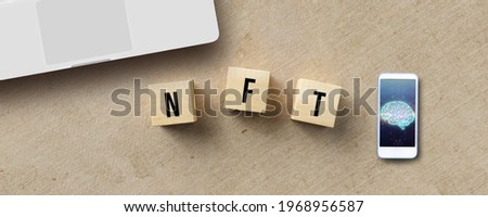 cubes with message NFT besides a smartphone with picture of a digital brain on paper background