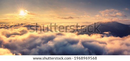 Aerial view of mountains in orange clouds at sunrise in summer. Mountain peak in fog. Beautiful landscape with rocks, hills, sky. Top view from drone. Mountain valley in low clouds. View from above Royalty-Free Stock Photo #1968969568