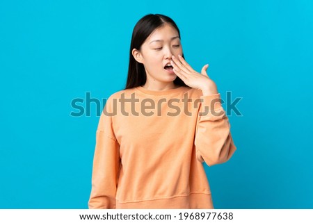 Young Chinese girl over isolated blue background yawning and covering wide open mouth with hand
