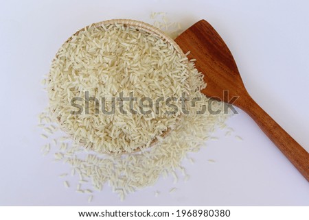 White rice raw in the wicker basket and wooden spoon isolated on white background closeup.