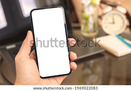 Man using smartphone mockup on background of laptop, home interior with alarm clock and homeplant, copy space 