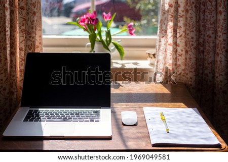 notebook, mouse and a pen with sheets on a table with flowers and a windows in bokeh