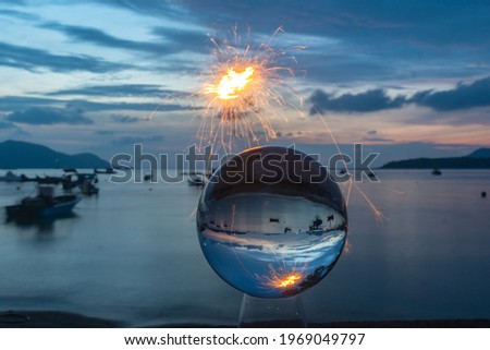 The sparkle of burning steel wool is the red line in the glass ball in twilight. 
With the sea and the morning light as a background.
