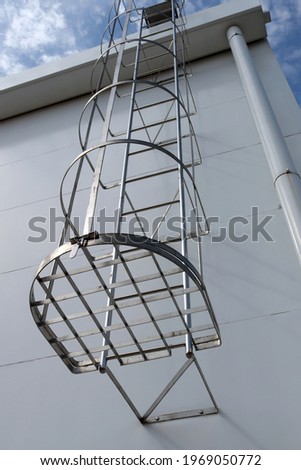 Aluminum cat ladder with cage. Outdoor fire escape, It is installed on the side of the building in the bottom view. Fire escape stairs outside the building. Royalty-Free Stock Photo #1969050772