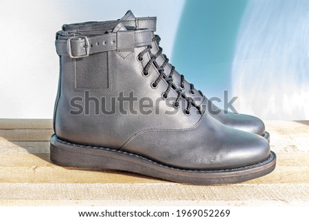 Black leather combat boots. Black men's leather army shoe. On wooden planks and turquoise background