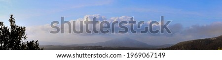 Panoramic photography of a group of rainy clouds over a majestic mountain behind a valley