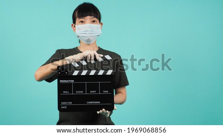Asian woman wear face mask hand hold black clapperboard or movie slate on mint green or Tiffany Blue background.Hand wear medical gloves.