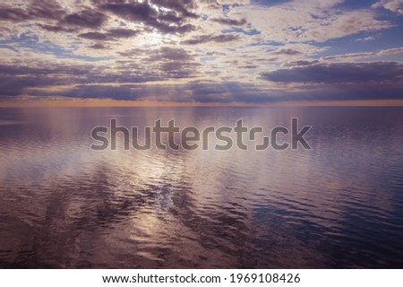 flying over the blue sea during sunset under white clouds that are reflected in the water