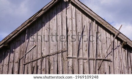 The end of an old wooden barn at the top of the roof ridge, gray, sun-faded old boards.