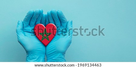 Doctors hands wearing surgical gloves holding Morocco flag heart