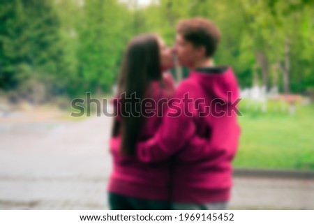  blurred the guy and the girl in pink oversize hoodies kiss in park.Image of young loving couple.relationship, date, love and fashion concept.romantic couple in pink hoodies in park.rear view 