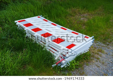 Red-and-white plastic portable barrier for fencing of hazardous areas for pedestrians and operating personnel stacked on the grass. Close-up.