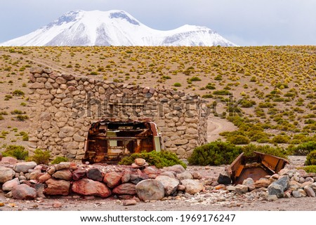 Rusty metal (car) parts in front of stone shed and volcano 