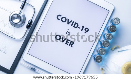 End of covid. Medical equipment: doctor stethoscope, hospital healthcare charts, syringe with needle and white tablet with text on screen. COVID is over concept