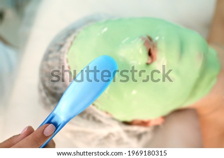 the cosmetologist applies the mask to the face with a spatula