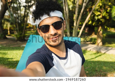 Selfie of Young Hispanic man on vacation relaxing by the pool - young man taking a selfie while spending time relaxing