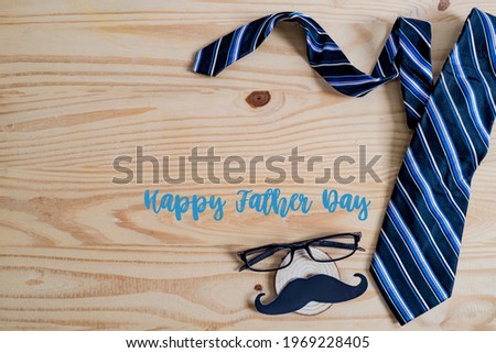 Happy Father's day concept. A black mustache paper, a blue necktie and glasses on wooden table.