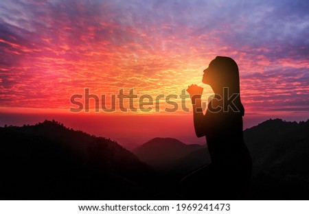 silhouette of women kneeling and praying over beautiful sunset with mountains Royalty-Free Stock Photo #1969241473
