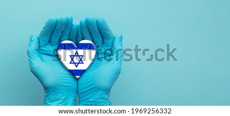 Doctors hands wearing surgical gloves holding Israel flag heart