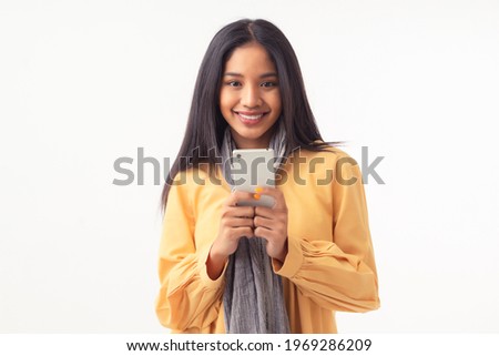 Portrait of young Asian woman with tan skin, wearing yellow blouses and grey scarf, holding mobile phone and presenting mobile application, happy emotion, isolated on white background