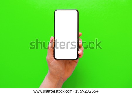 Person holding mobile phone with empty white screen on green background