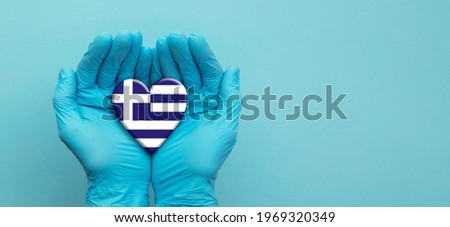 Doctors hands wearing surgical gloves holding Greece flag heart