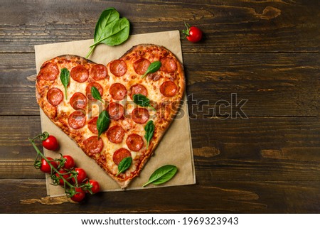 Heart shaped pizza pepperoni on dark wooden background with spinach and tomatoes cherry