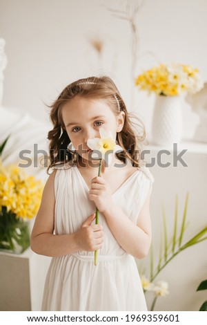 pretty little girl in white dress holding one narcissus in hands