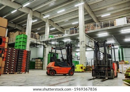 Warehouse and storage for packing and stocks of goods. Old rusty forklifts are in an empty warehouse with no people. In the background are boxes and pallets for packing fresh fruits and vegetables