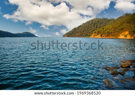 Laguna of azure Aegean Sea with lush mountains, fluffy clouds in blue sky, summer weather. Nature landscape in East Turkey. Concept of relaxation, vacation, recreation and travel. Copy space for site