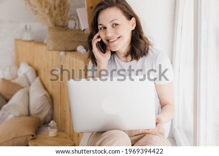 Smiling young Caucasian woman record digital audio message on smartphone in modern flat