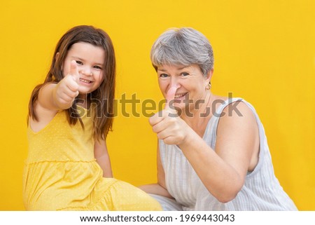 Grandmother and child show thumb up and smile on yellow background