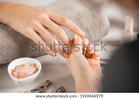 Close up of beautician hands doing hand treatment at nail salon. Woman holding the finger of customer during manicure. Detail of hands of manicurist massaging client fingers in manicure salon. Royalty-Free Stock Photo #1969446979
