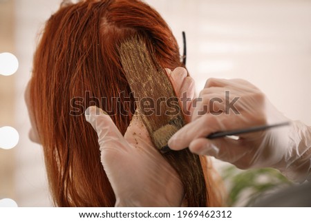 Professional hairdresser dyeing woman's hair with henna on blurred background, closeup