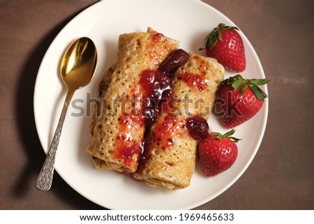 Pancakeshin roll with strawberry jam on plate. Pancakes poured berry jam and decorated fresh strawberries. Top view.