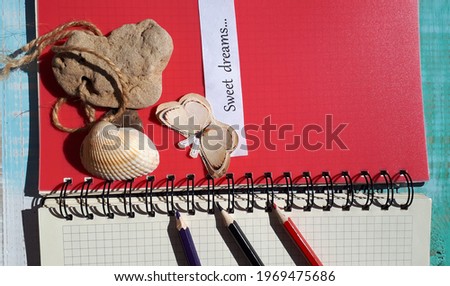 A notebook with a red page, colored pencils, a stone, and a paper butterfly. Lettering on paper: sweet dreams