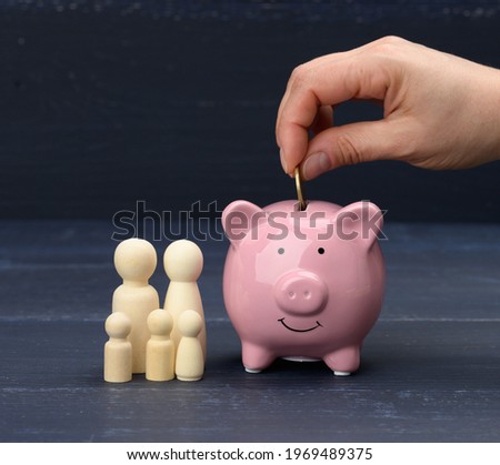 wooden family figurines and pink ceramic piggy bank on blue background. Concept of accumulating cash for buying a house and a car, money in the bank at interest, safe storage