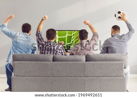 Sofa experts. Back view of male friends gathered at home to watch a football match sitting on the couch in front of the big screen TV. Men actively support their favorite team and comment on the match Royalty-Free Stock Photo #1969492651