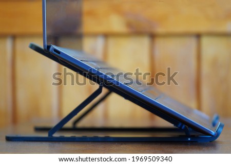 A modern slim silver laptop or ultrabook mounted on a portable holder stand against a wooden background. Side view. The concept of modern gadgets. Close-up