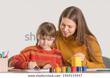 Drawing teacher giving private art lessons to little girl on light background