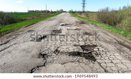 The texture of cracked old asphalt in need of repair. The road is full of holes and potholes.                     Royalty-Free Stock Photo #1969548493