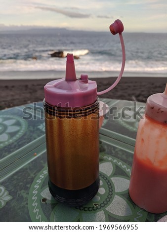 a bottle of soy sauce and sauces on a beach side table.