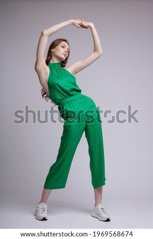 High fashion photo of a beautiful elegant young woman in a pretty juicy green jumpsuit, sneakers posing over white, soft gray background. Studio Shot. Full length portrait