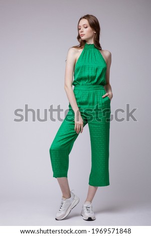 High fashion photo of a beautiful elegant young woman in a pretty juicy green jumpsuit, sneakers posing over white, soft gray background. Studio Shot. Full length portrait Royalty-Free Stock Photo #1969571848