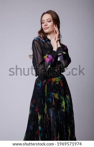 High fashion photo of a beautiful elegant young woman in a pretty black long skirt and shirt with colored patterns, sneakers posing over white, soft gray background. Studio Shot.