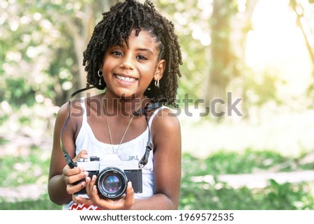 portrait of a young african american toddler girl holding an old camera and looking at camera. childhood happiness and learning concept.