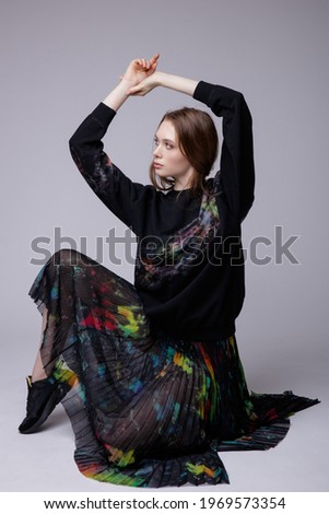 High fashion photo of a beautiful elegant young woman in a pretty black long skirt and jacket with colored patterns, sneakers posing over white, soft gray background. Studio Shot.