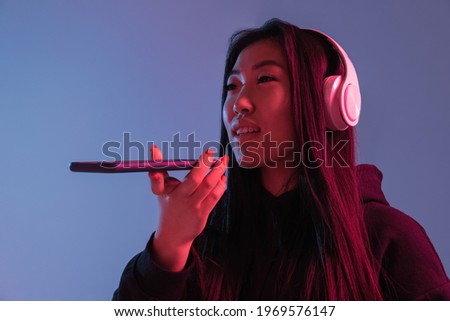 Talking. Asian young woman's portrait on blue studio background in neon light. Beautiful female model in casual style. Concept of human emotions, facial expression, youth, sales, ad.
